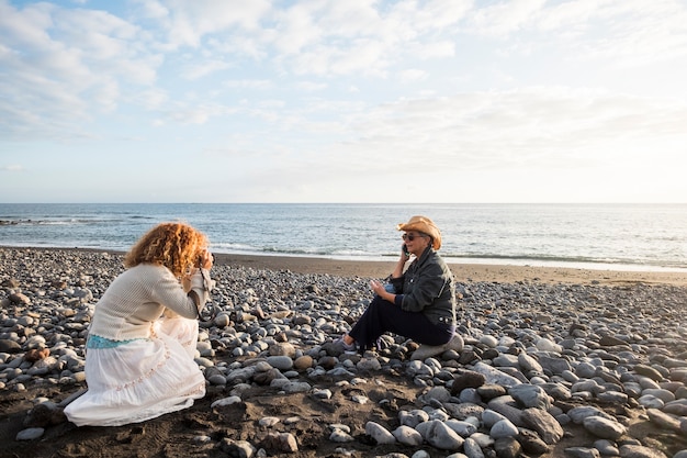 Photo photoshooting with two females. one photographer and a mature woman speaking at the phone to represent a nice lifestyle on the beach. stock and advertising concept work