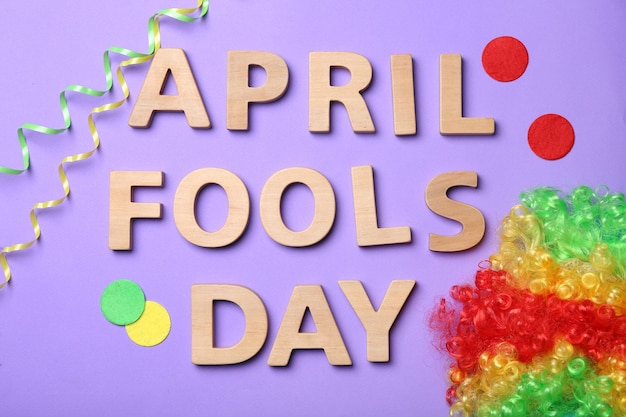 Phrase April fools day and rainbow wig on color background