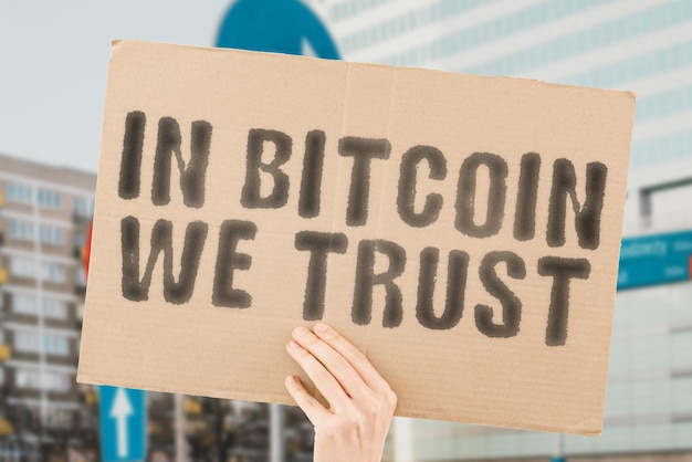 The phrase In Bitcoin we trust is on a banner in men's hands with blurred background Code Data