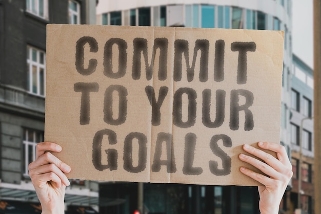 The phrase Commit to your goals is on a banner in men's hands with blurred background Career Plan Mission Behavior Efficiency Commit Achieve Strong Goal Strength Motivation Condition