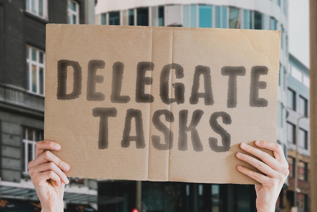 The phrase Delegate tasks on a banner in men's hands with blurred background Office Develop Effect Organize Organized Multitask Help Teamwork Successful Success Accept Function Goal