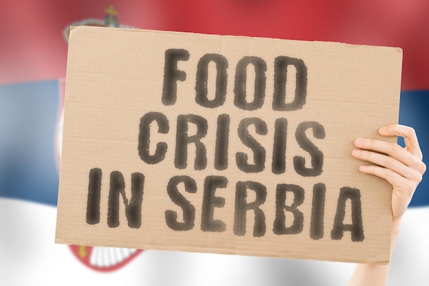 The phrase Food crisis in Serbia is on a banner in men's hands with a blurred Serbian flag in the background Crisis Finance Life Nutrition Bread Disaster Collapse Social issue