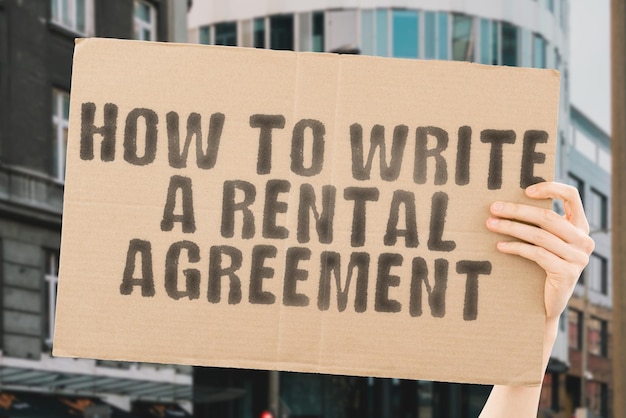 The phrase " How to Write a Rental Agreement " on a banner in men's hand with blurred background. Estate agent. Housing tenants. Living space. Place. Habitation. Tenement. Tenement. Room