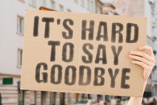 The phrase It's hard to say goodbye is on a banner in men's hands with blurred background Reliability Important Relation Failure Afraid Maintenance Fatherhood Emotions Sadness Protect