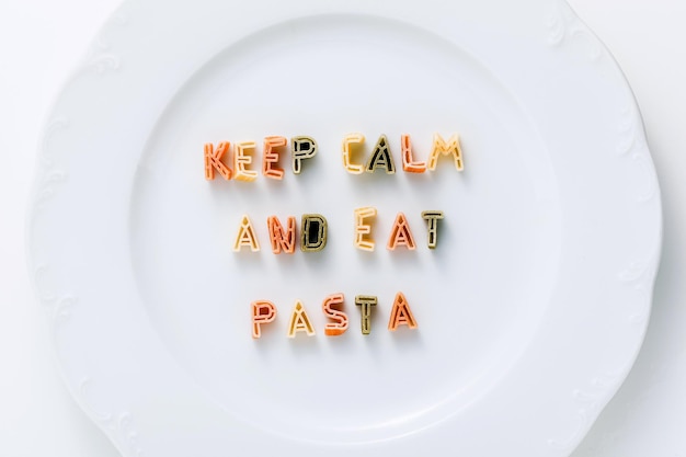 Phrase KEEP CALM AND EAT PASTA from dry multicolored pasta on a white plate