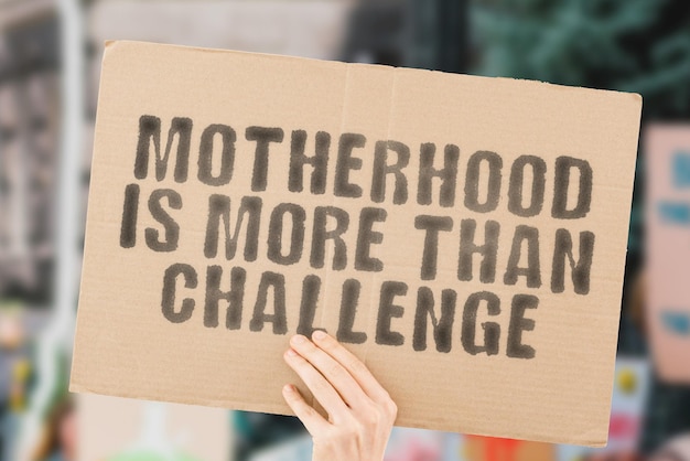 The phrase Motherhood is more than challenge on a banner in men's hand with blurred background Parent Parenthood Family Education Problem Hard Child Children