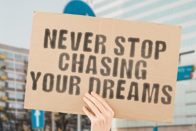 The phrase  Never stop chasing your dreams  on a banner in mens hand with blurred background Job