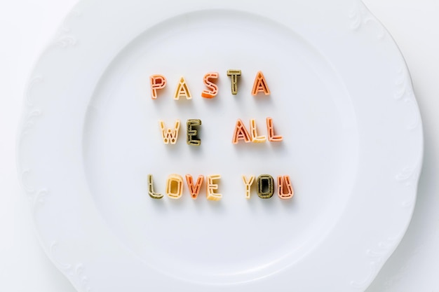 Phrase PASTA WE ALL LOVE YOU from dry multicolored pasta on a white plate