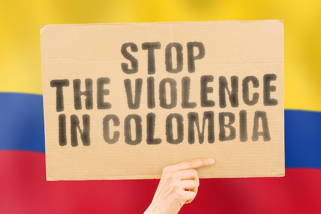 The phrase Stop the violence in Colombia is on a banner in men's hands with a blurred Colombian flag in the background Sad Rights Security Social Stress Combat Hate Cruelty