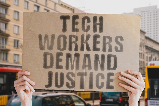 The phrase  Tech workers demand justice  on a banner in mens hand with blurred background Job