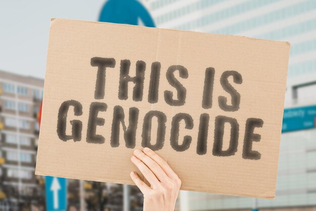 The phrase This is genocide on a banner in men's hands with blurred background Bury Secret Hidden Psychopath Disaster Hurt Satanic Deadly Threat Violence War World Blood Attack