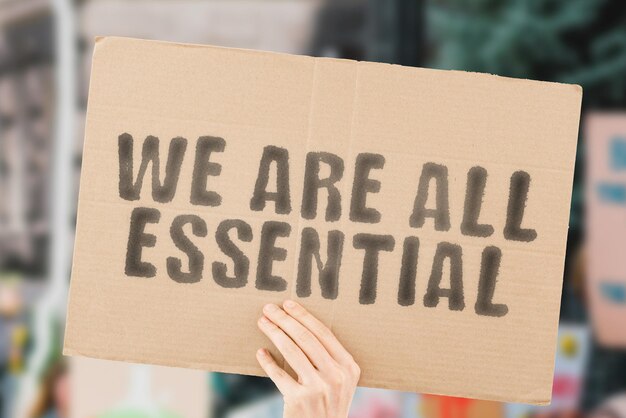 The phrase We are all essential on a banner in men's hand with blurred background Job Profession Equality Speciality Occupation Economical crisis Money