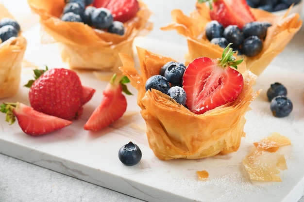 Phyllo or filo pies with fresh berries strawberries and blueberries cheese filling topped with fresh mint on white plate Homemade Filo pastry paskets Delicious filo pastry dessert