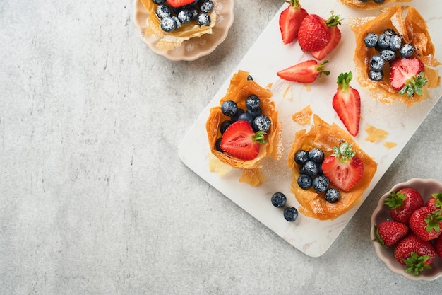 Phyllo or filo pies with fresh berries strawberries and blueberries cheese filling topped with fresh mint on white plate Homemade Filo pastry paskets Delicious filo pastry dessert