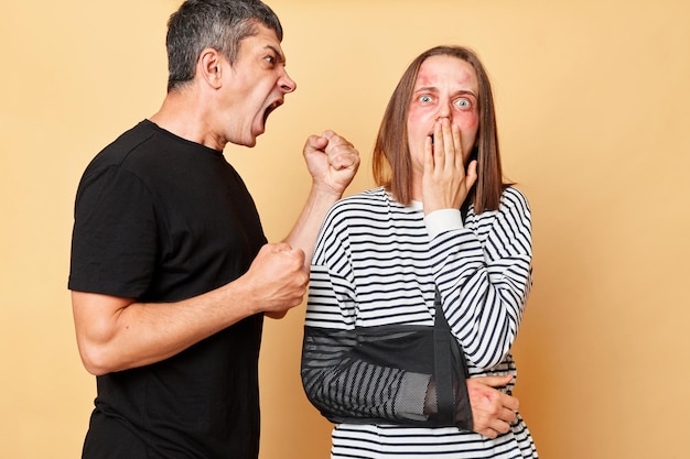 Physical punishment Violent screaming with negative emotions man and woman with bruise suffering from home violence and beatings isolated over beige background