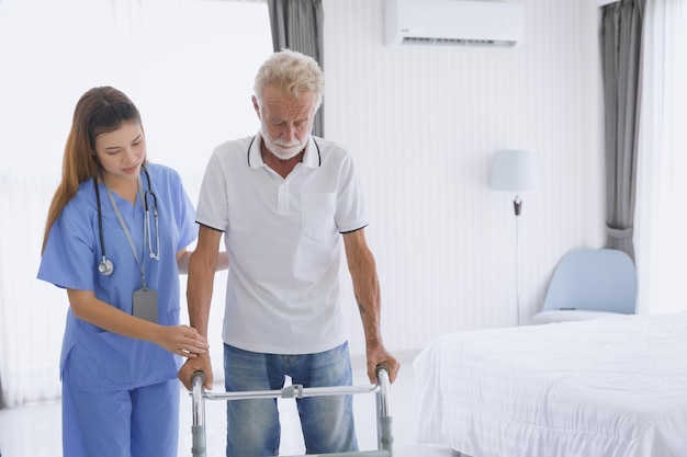 Physical therapist nurse supporting patient elderly senior old man practicing leg muscle recovery with walker equipment