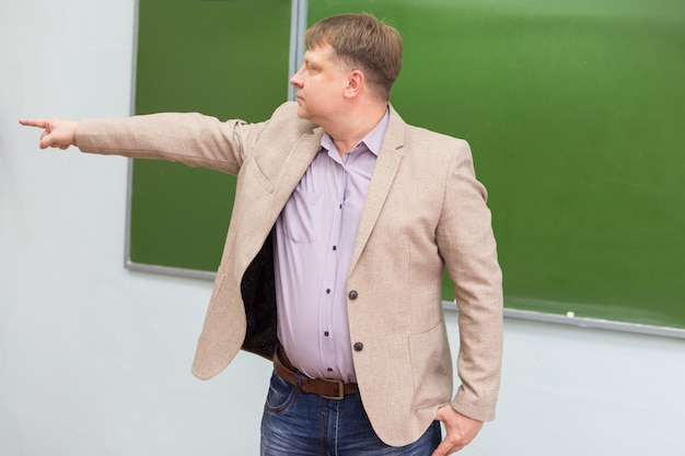 The physics teacher at the blackboard shows the student the exit from the classroom with a hand gesture