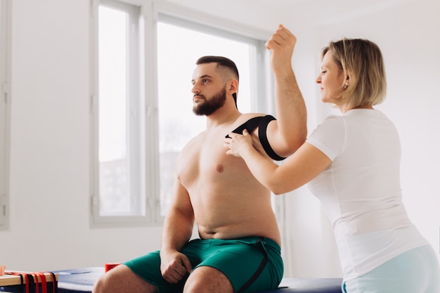 Physiotherapist Applying Kinesio Tape To Patients Injured Shoulder