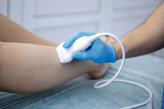 Physiotherapist is applying ultrasound therapy on the legs of a female patient.