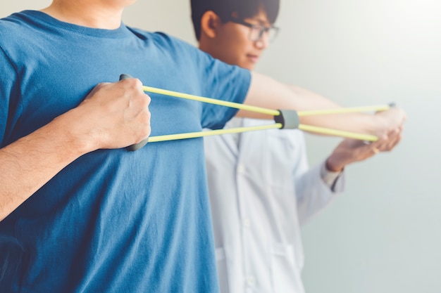 Physiotherapist man giving resistance band exercise treatment About Arm and Shoulder of athlete male patient Physical therapy concept