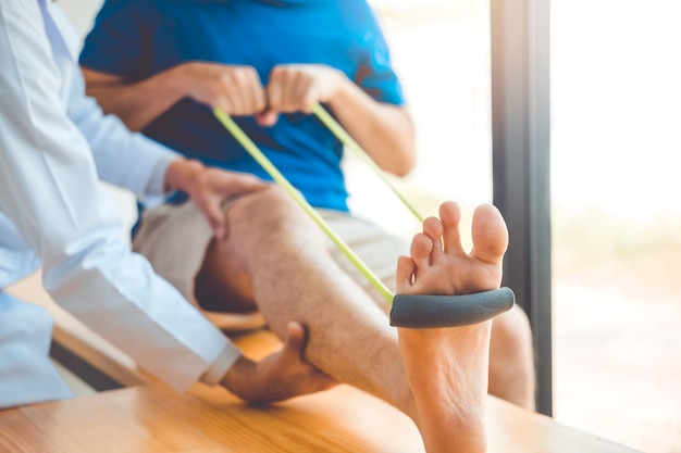 Physiotherapist man giving resistance band exercise treatment About knee of athlete 