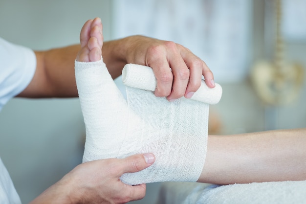 Physiotherapist putting bandage on injured feet of patient