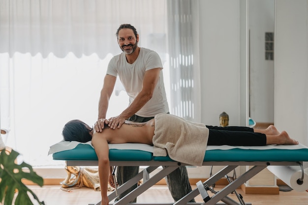 Physiotherapist smiling on camera while massaging a young patient