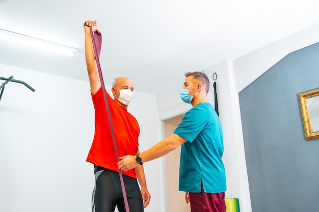 Physiotherapist with face mask stretching the patient's neck with a rubber band Physiotherapy with protective measures for the Coronavirus pandemic COVID19 Osteopathy sports quiromassage