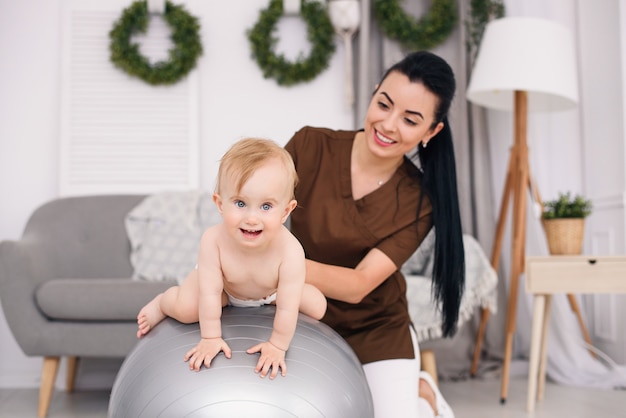 Physiotherapist with happy baby doing exercises with gymnastic ball at medical room. Healthcare and medical concept.