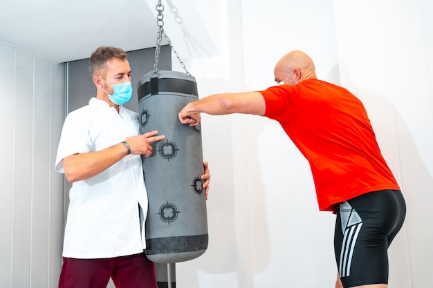 Physiotherapist with mask together with the patient on the punching bag Physiotherapy with protective measures for the Coronavirus pandemic COVID19 Osteopathy sports quiromassage