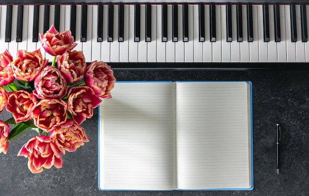 Piano bouquet of tulip flowers and notepad on a dark background top view