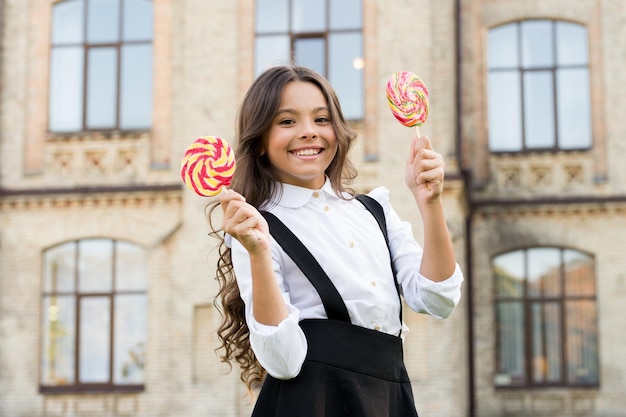 Photo picking flavour is hardest part schoolgirl choosing sweets happy kid with sweet candy kid child holding lollipops candy outdoors happy kid with candy school nutrition calories and energy