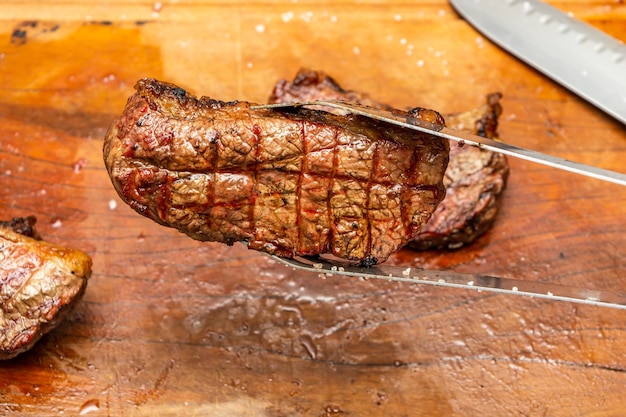 picking up beef steak of picanha with metallic tongs