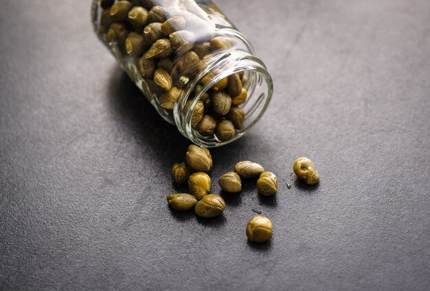 Pickled capers in a jar on dark wooden