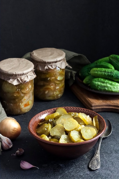 Pickled cucumber salad in a bowl and jars on black background