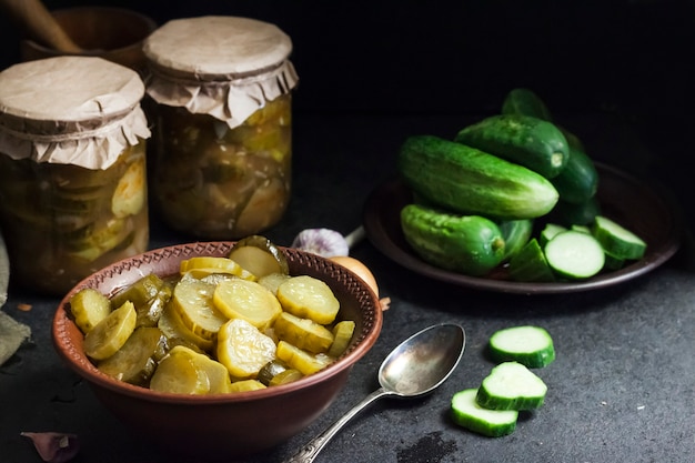 Pickled cucumber salad in a bowl and jars on black background