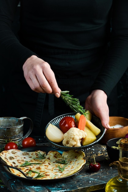 Pickled cucumbers, tomatoes, onions and cabbage on a plate in the hands of a chef on a black background.