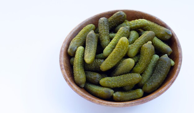 Pickled gherkins or cucumbers in wooden bowl on white background.