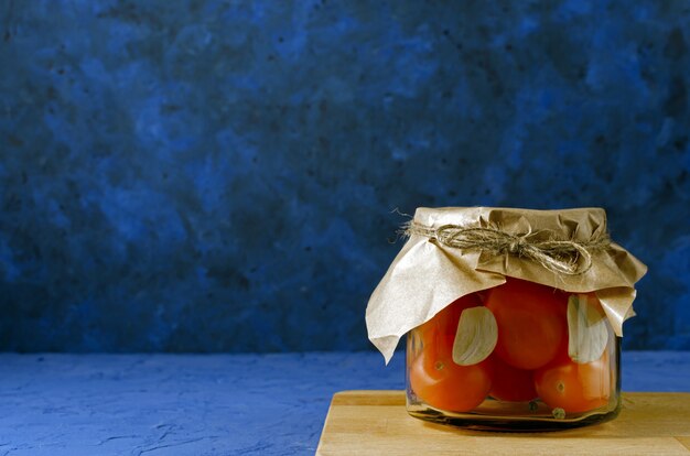 Pickled tomatoes in jar on classic blue background. Top view. Copy space. Canned and preserved vegetables. Ingredients for vegetables preserving. Healthy fermented food concept