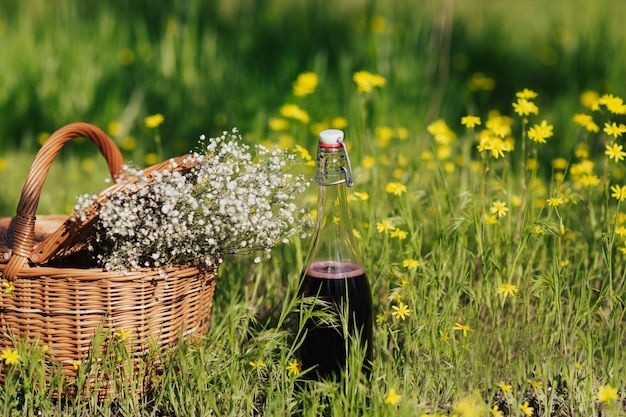 picnic basket with flowers and bottle with wine on the green grass