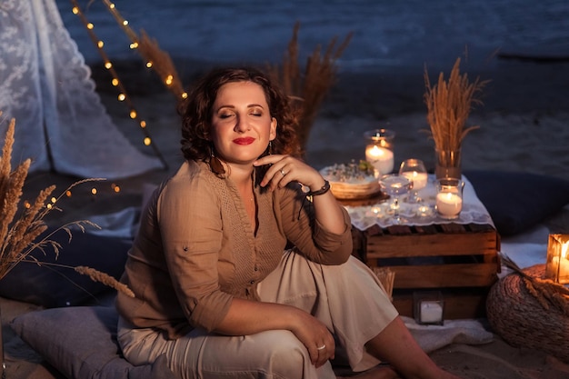 Picnic in the evening at sunset on the sandy shore of the sea or ocean decor in boho and rustic style portrait of a beautiful woman at a picnic