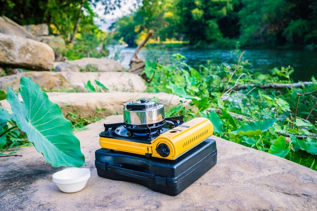 Photo picnic gas stove and aluminum teapot for boiling water during camping near the river