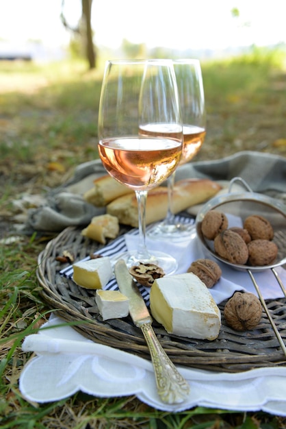 Picnic theme rose wine cheese baguette and nuts on wicker tray outdoors