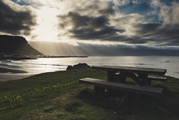 A picnic wooden table with gorgeous view at ocean with sun shining through the clouds in Iceland Place for rest travel concept