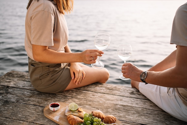 Picnic of a young couple on the pier near the lake, glasses of wine