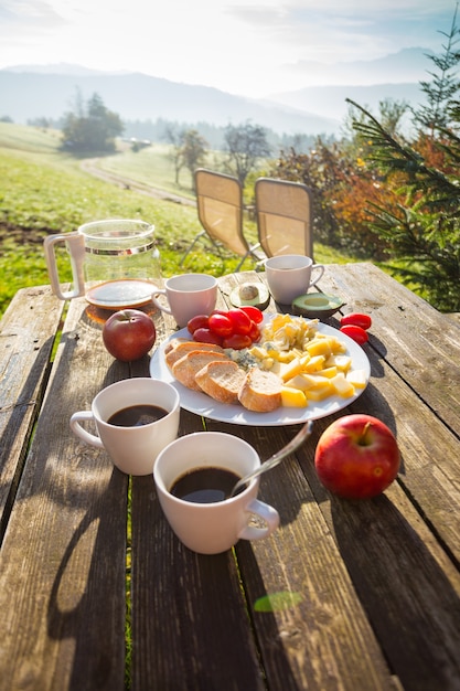 Picnicin on a farm.  morning in the mountains. cheeses, baguette, tomatoes, avocado, coffee on a wooden table