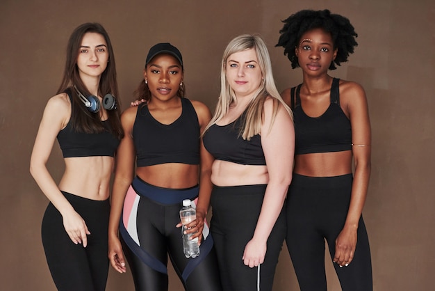 Picture after hard workout. Group of multi ethnic women standing  against brown space