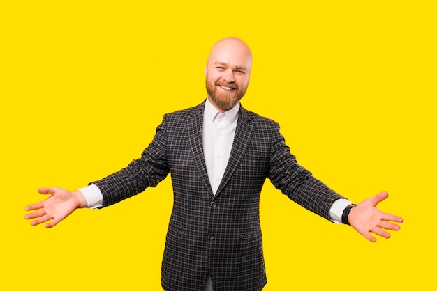 Picture of a bearded businessman smiling at the camera while he wants a hug over yellow wall