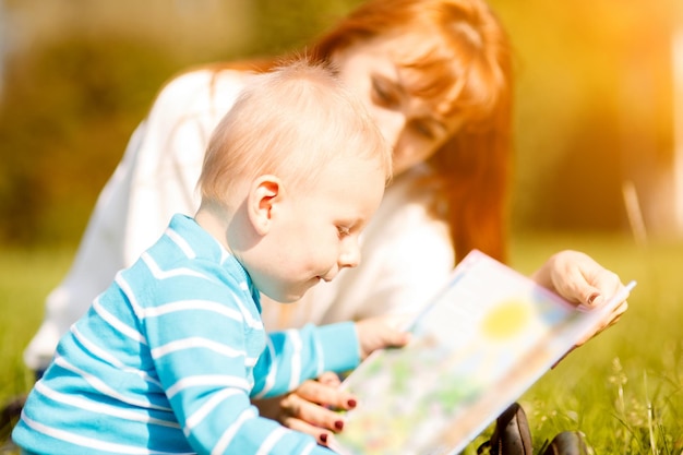 Picture of beautiful woman with son sitting down on green grass field and read fairytale in park