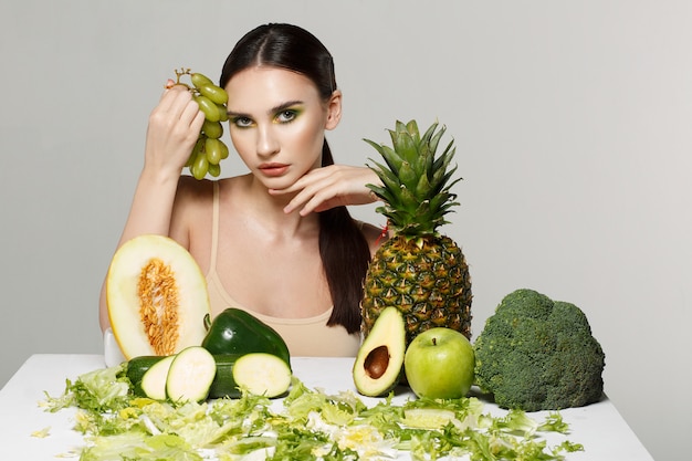 Picture of beautiful young brunette woman with fruits and vegetables on the table